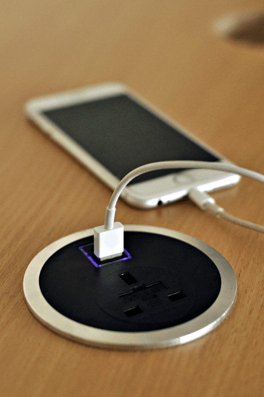 Phone being charged by the Flon In-Desk Power Outlet with USB Smart Charge.