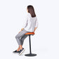 Woman sitting on the Cloonch Sit-Stand Stool with red seat